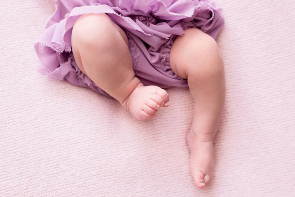 παχουλός πόδια από ένα νεογέννητο κορίτσι σε μια λιλά φούστα, νέος μπαλαρίνα χορεύτρια, δάχτυλα στα πόδια της, χοροί κινήσεις, ροζ φόντο, μέρος για το κείμενο - Φωτογραφία, εικόνα