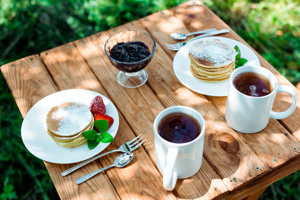 overhead view of tasty pancakes with organic strawberries near cups with tea  - Zdjęcie, obraz