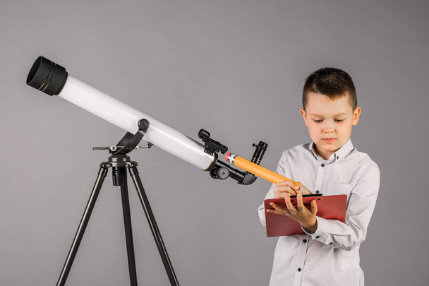 young astronomer looks through a telescope and writes in the tab - Фото, изображение