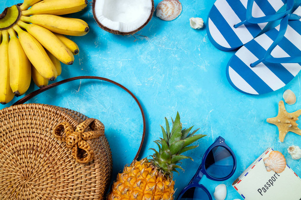 Zomer vrouwelijke mode strand accessoires flip flop, bamboe tas, zonnebril en tropische vruchten op blauwe achtergrond. Reis-, vocaties-, reis-en zomer rust concept - Foto, afbeelding