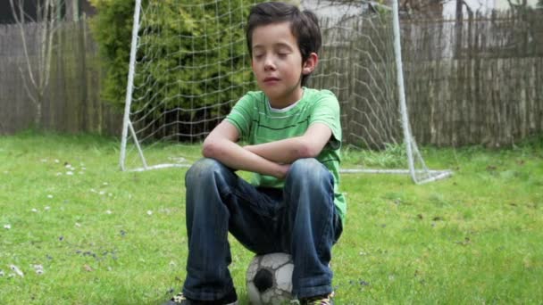 Trauriger Junge sitzt auf Fußball - Felvétel, videó