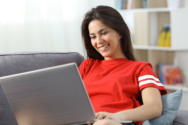 Boldog tizenéves lány használ egy laptop-ra egy kanapén otthon - Fotó, kép
