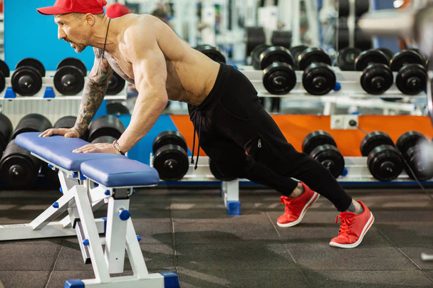 Strong sporty man doing push-ups on bench during workout in gym - Photo, Image