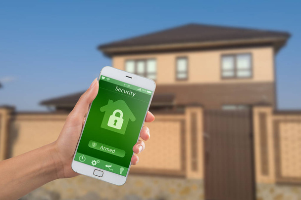 Smartfon z domową aplikacją bezpieczeństwa w dłoni na tle budynku - Zdjęcie, obraz