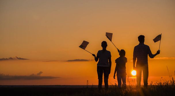 Rodzina z dzieckiem macha nas flagi o zachodzie słońca, widok z tyłu - Zdjęcie, obraz