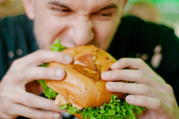 Ο άνθρωπος σε ένα εστιατόριο που τρώει ένα χάμπουργκερ, πεινάει και έχει μια καλή μπουκιά. επιλεκτική εστίαση - Φωτογραφία, εικόνα