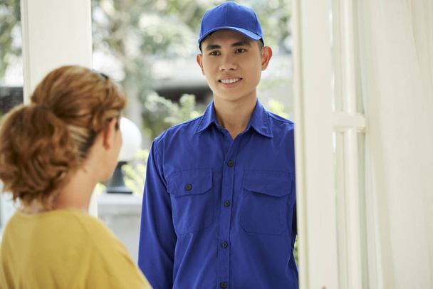 Jeune réparateur asiatique vient à la maison de la femme, il debout et souriant tandis que la femme ouvre la porte de sa maison
 - Photo, image