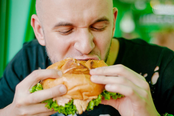 Mann in einem Restaurant isst einen Hamburger, er ist hungrig und hat einen guten Bissen. Selektiver Fokus - Foto, Bild