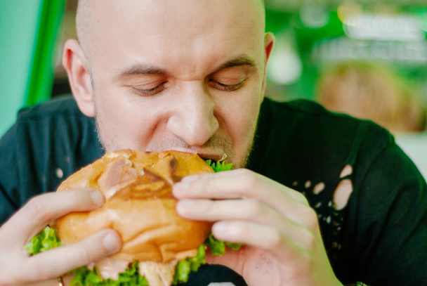 Bir restoranda hamburger yiyen adam, aç ve iyi bir ısırık içiyor. seçici odaklama - Fotoğraf, Görsel