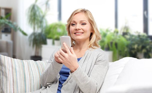 smiling woman with smartphone texting at home - Fotoğraf, Görsel