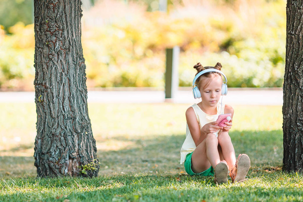 Little adorable girl listening music in the park - Fotografie, Obrázek