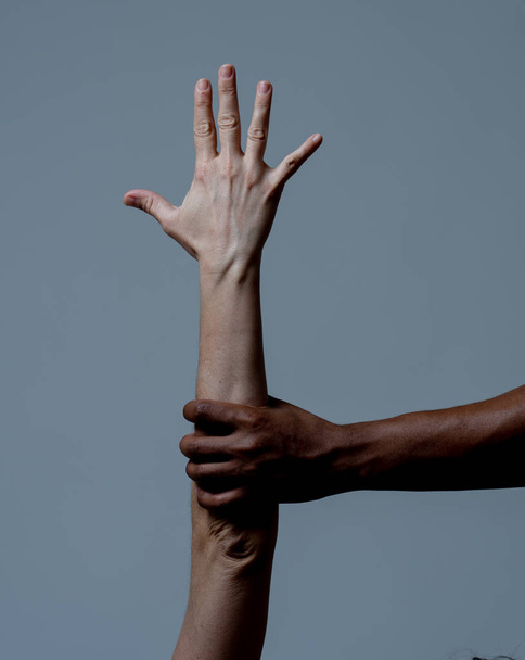 Black African American hand holding white skin arm. Conceptual image of Humanitarian campaign in helping refugees and stop racism issues. World unity cooperation Tolerance and human rights concept. - Fotoğraf, Görsel