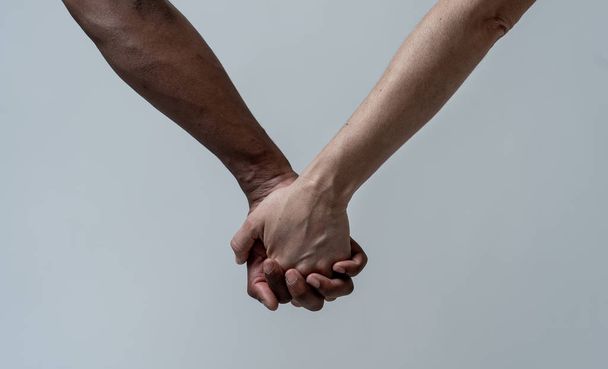 Багаторасова пара тримає руки разом в любові. Білі та чорні шкіряні руки тримаються разом. Концептуальний образ світової єдності міжрасової любові та розуміння в терпимості та різноманітності
. - Фото, зображення
