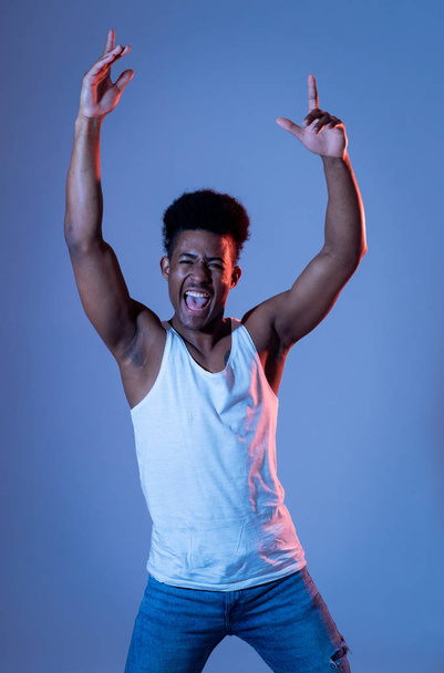 Portrait of inspired cool african american teenager man dancing feeling the music and enjoying life on blue moody disco neon light background. In People, Youth Party night lifestyle. Studio shot. - Valokuva, kuva