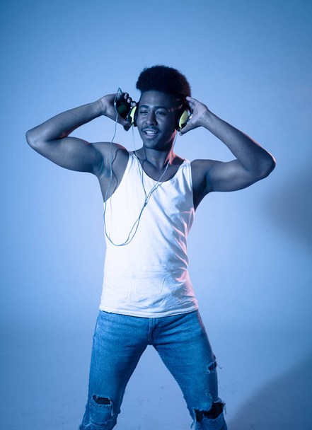 Strong african american young dancer man listening to music online dancing and singing with headphones. Artistic portrait with disco dance floor neon light in Internet Music and technology concept. - Φωτογραφία, εικόνα