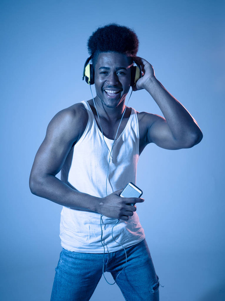 Strong african american young dancer man listening to music online dancing and singing with headphones. Artistic portrait with disco dance floor neon light in Internet Music and technology concept. - Foto, immagini