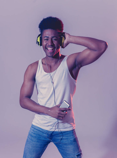 Strong african american young dancer man listening to music online dancing and singing with headphones. Artistic portrait with disco dance floor neon light in Internet Music and technology concept. - Foto, afbeelding