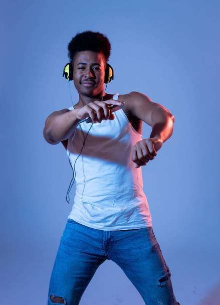 Strong african american young dancer man listening to music online dancing and singing with headphones. Artistic portrait with disco dance floor neon light in Internet Music and technology concept. - 写真・画像