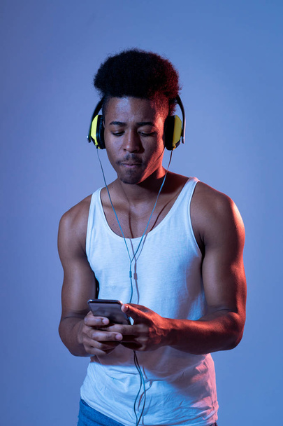 Strong african american young man listening to music in smartphone app looking for best song online with headphones singing and dancing. Portrait with disco dance floor light in Music and technology. - Фото, зображення