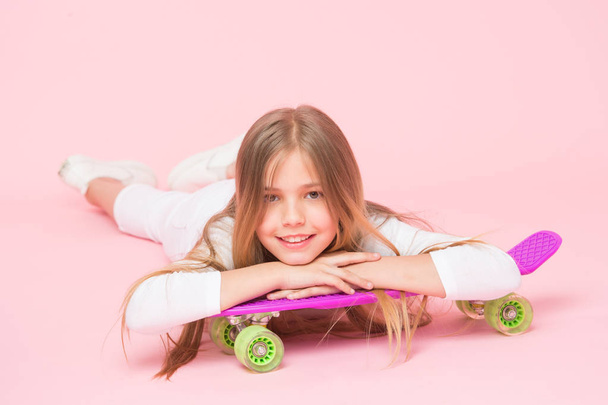 Trendy girl. Ride penny board and do tricks. Girl likes to ride skateboard. Active lifestyle. Girl having fun with penny board pink background. Kid adorable child long hair adore ride penny board - Photo, image