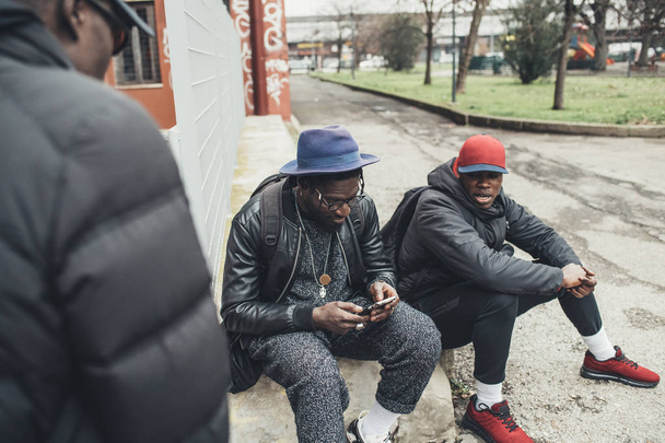 τρεις Αφρικανοί φίλοι κάθονται σε εξωτερικούς χώρους και αναζητούν το smartphone - Φωτογραφία, εικόνα
