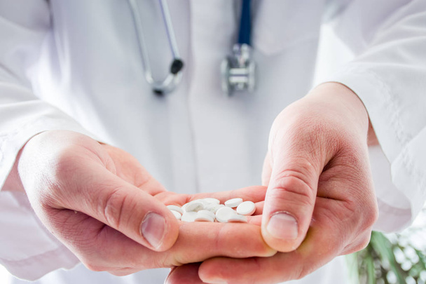 Doctor keeps in folded palms pills in foreground with focus on drugs, on background blurred body in white robe with phonendoscope. Concept pharmacological treatment, drug of last resort, accessibility - Foto, Imagem