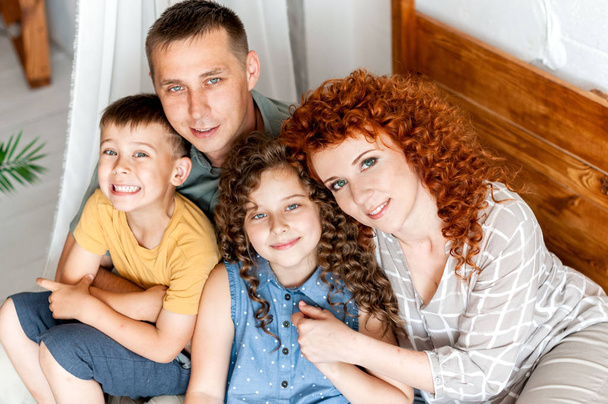 Retrato de uma jovem família feliz com duas crianças no quarto, cabelo encaracolado
 - Foto, Imagem