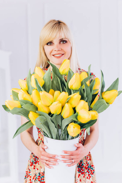 A young girl blonde with a bouquet of yellow tulips in her hands meets spring. - Фото, изображение