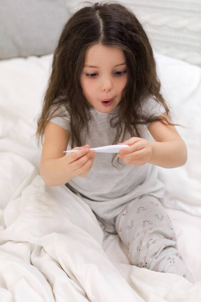 Sick little girl lying in bed with thermometer - 写真・画像