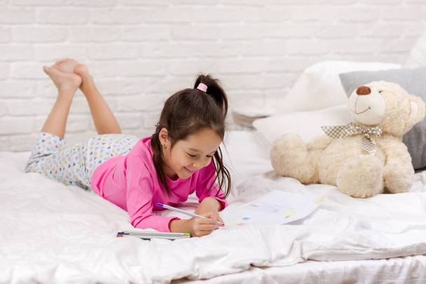 aranyos kislány rajz képek mellett fekve az ágyban - Fotó, kép