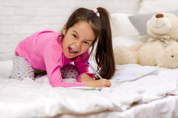 cute little girl drawing pictures while lying on bed - Foto, imagen