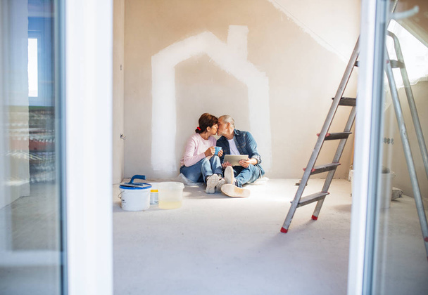 Kıdemli çift yeni evde duvarlar boyama, öpüşme. Tehcir kavramı. - Fotoğraf, Görsel