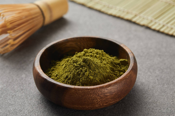 selective focus of bamboo whisk and green matcha powder in wooden bowl on grey table with copy space - 写真・画像