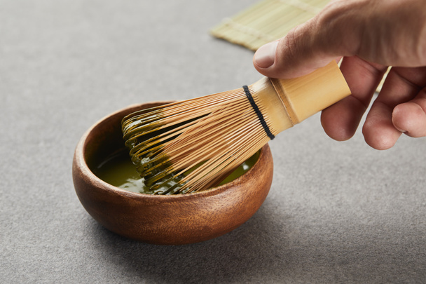 selective focus of man holding bamboo whisk in wooden bowl with green matcha - Foto, afbeelding