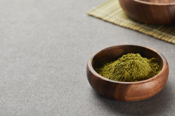selective focus of green matcha powder in wooden bowl on grey table with copy space - Foto, Imagen