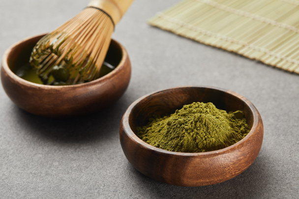 selective focus of green matcha powder and bamboo whisk in wooden bowl with tea - Zdjęcie, obraz