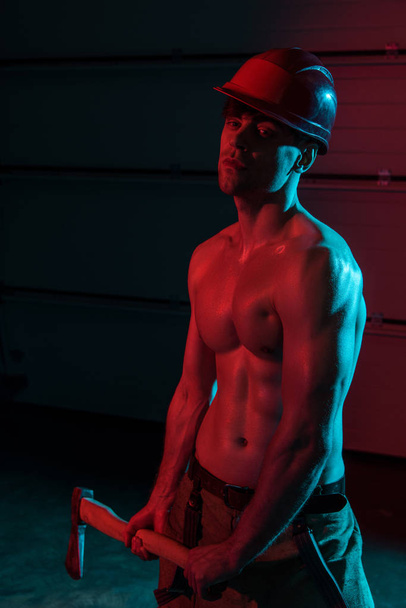 sexy shirtless fireman holding flat head axe in darkness - Fotó, kép