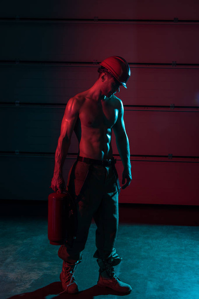 полный вид сексуального пожарного без рубашки, держащего огнетушитель в темноте
 - Фото, изображение