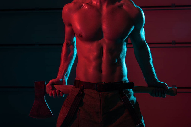 partial view of sexy shirtless fireman holding flat head axe in darkness - Foto, immagini