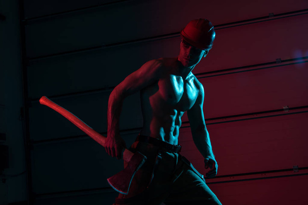 sexy shirtless fireman in protective hardhat holding flat head axe in darkness - Φωτογραφία, εικόνα