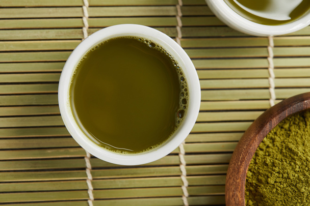 top view of white cups with green tea near matcha powder in wooden bowl - Photo, image