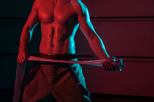 cropped view of shirtless fireman holding fire hose in darkness - Foto, immagini