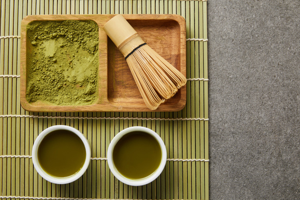 vue du dessus de la poudre de matcha vert avec fouet de bambou sur planche en bois près des tasses blanches avec thé vert sur le tapis de table
 - Photo, image