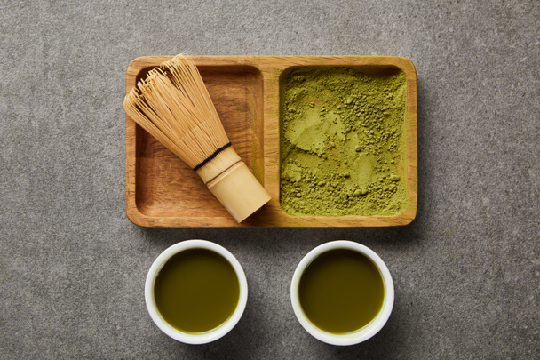 top view of bamboo whisk and matcha powder on wooden bowl near white cups with green tea - Photo, Image