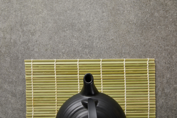 top view of green bamboo table mat with black teapot on grey surface - 写真・画像