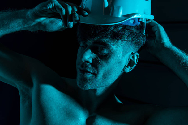 sexy shirtless fireman touching protective hardhat in darkness - Photo, Image