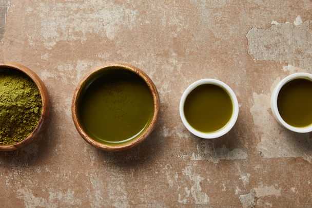 Top View van matcha poeder, Bowl en kopjes met groene thee op verouderd oppervlak - Foto, afbeelding