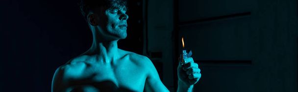 panoramic shot of sexy shirtless man holding lighter with closed eyes in darkness - Фото, изображение