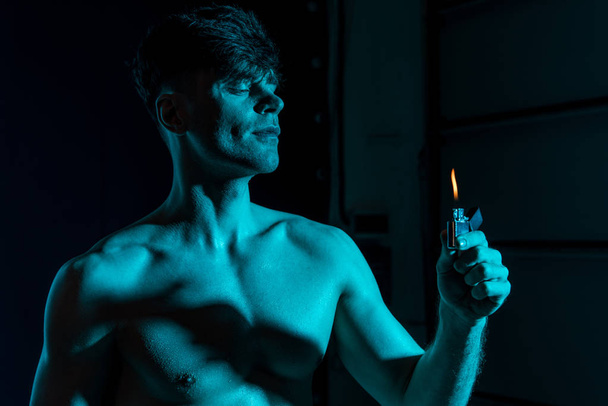 σέξι ημίγυμνος μυώδης άνθρωπος κρατώντας αναπτήρα στο σκοτάδι - Φωτογραφία, εικόνα