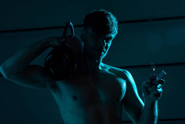 sexy shirtless fireman holding fire extinguisher and lighter in darkness - Photo, Image